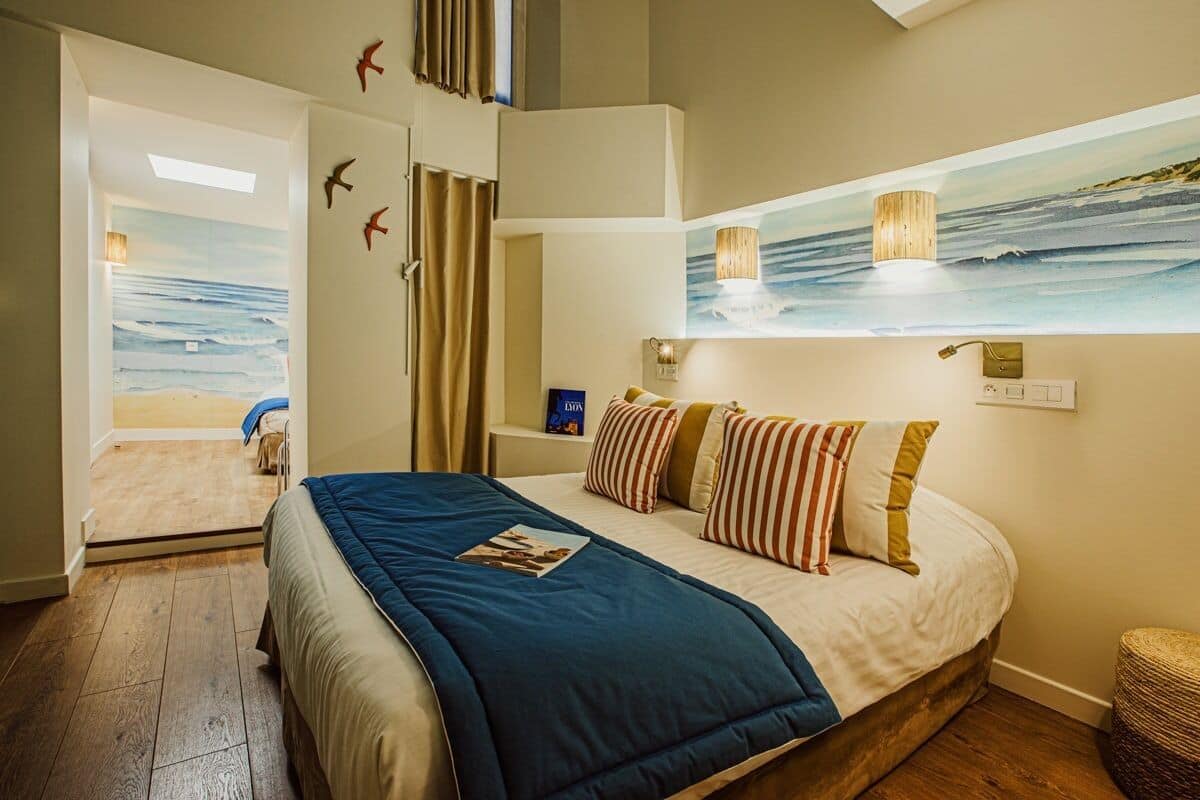A bedroom with a bed, a painting of the ocean, and a view of the beach.