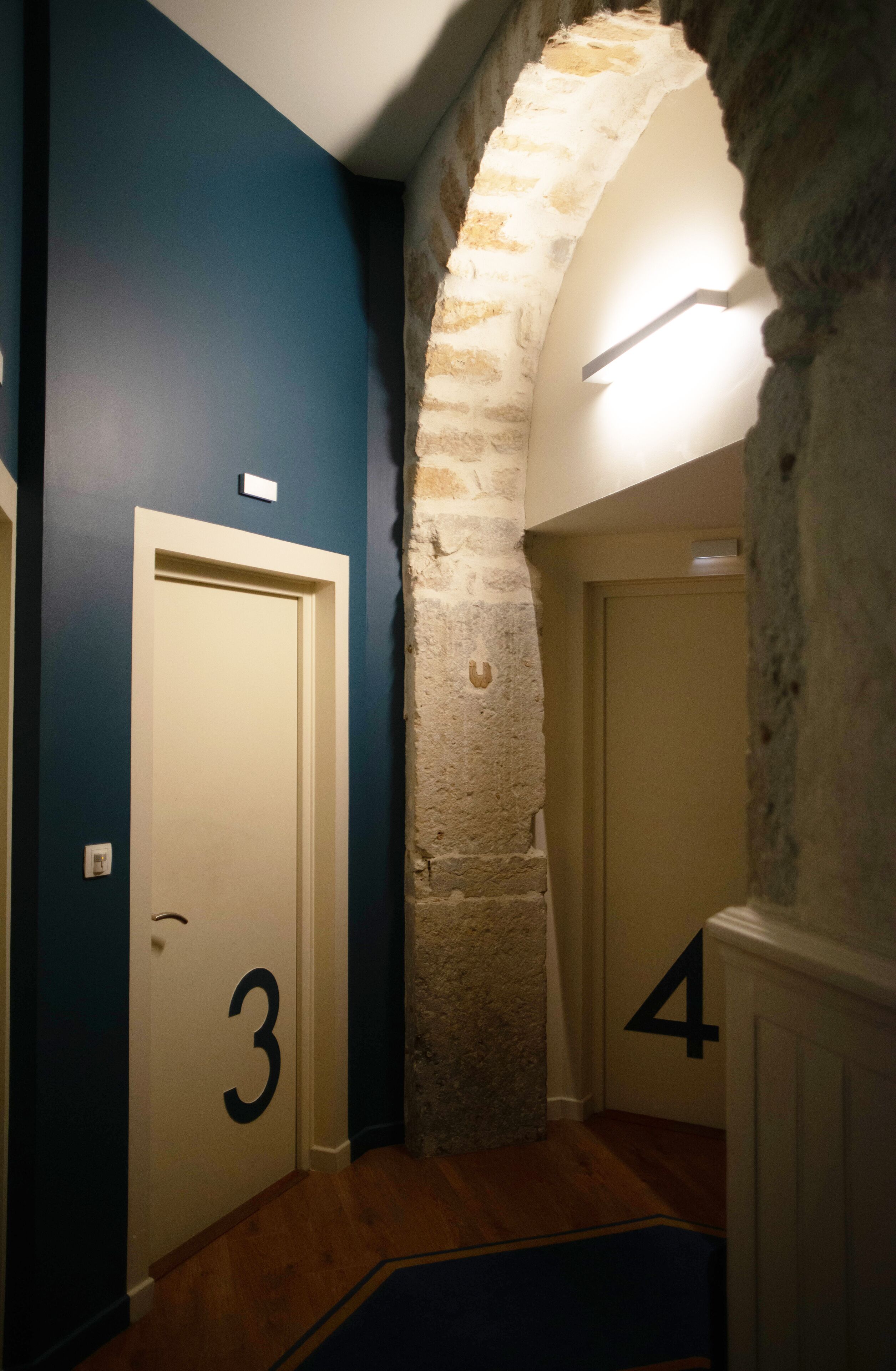 A hallway with doors numbered 3 and 4, a stone archway, and a blue wall.