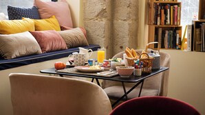 A cozy living room with a sofa, a coffee table with breakfast items, and a bookshelf filled with books. - HOTELO Lyon Charité (Lyon)