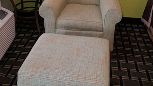 A room with a green wall, a small round table, a chair, and a matching ottoman. - American Inn (Columbia)