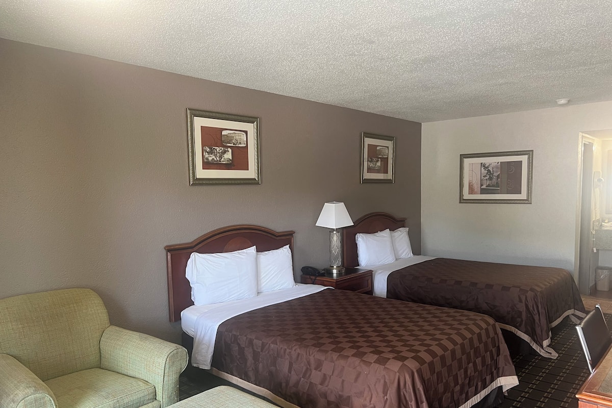 A hotel room with two beds, a chair, and framed pictures on the walls.