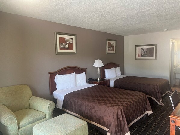 A hotel room with two beds, a chair, and framed pictures on the walls.