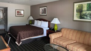 A hotel room with a bed, two bedside lamps, a sofa, a small table, and framed pictures on the walls. - American Inn (Columbia)