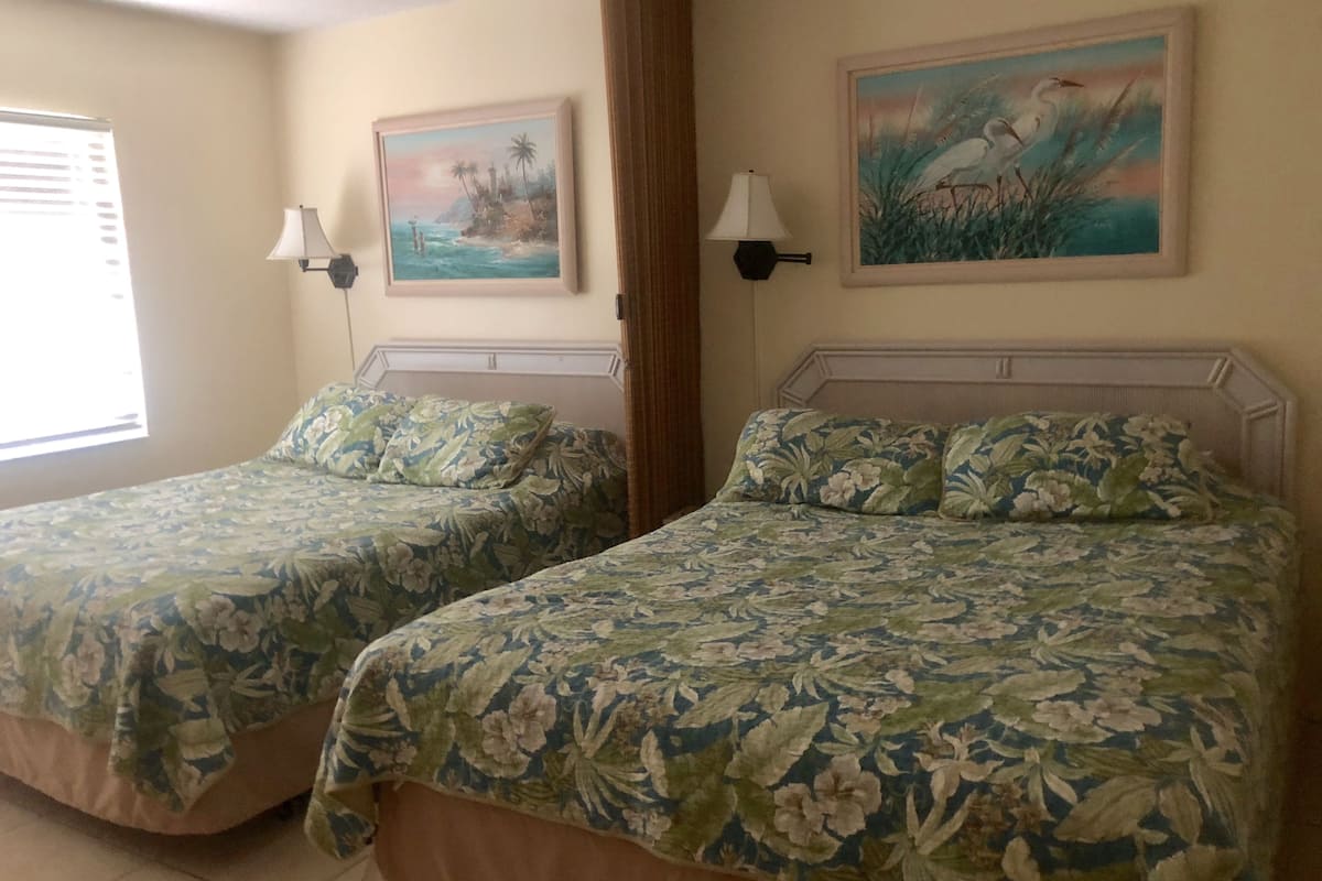Two twin beds with floral bedding, a painting of a beach scene, and a lamp on each side.
