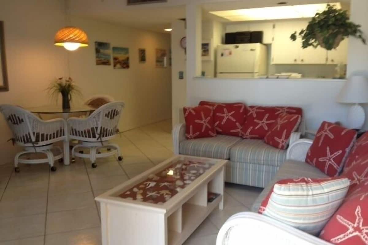 A living room with a sofa, armchairs, a coffee table, and a dining area with chairs and a table.