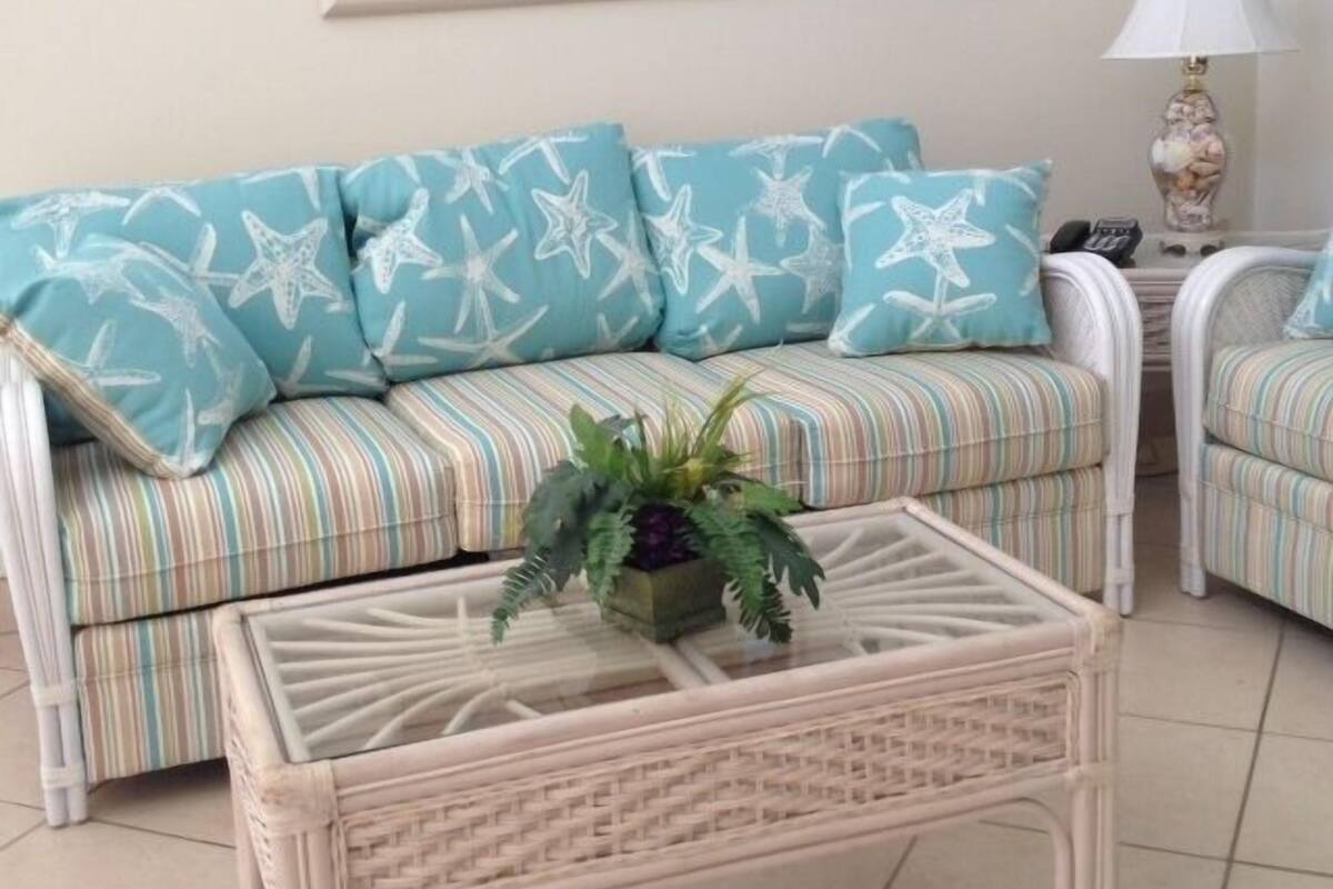 A room with a sofa featuring starfish patterns, a striped cushion, and a glass coffee table with a plant.