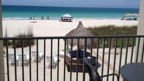 A beach view from a balcony with lounge chairs, a thatched umbrella, and a tent on the sand. - Coconuts Beach Resort (Holmes Beach)