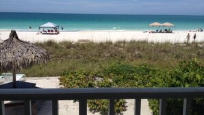 A beach view with a thatched umbrella, lounge chairs, and a clear blue sky. - Coconuts Beach Resort (Holmes Beach)