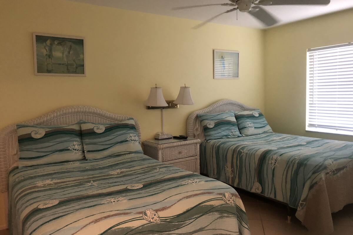 A bedroom with two beds, a ceiling fan, and a window with blinds.