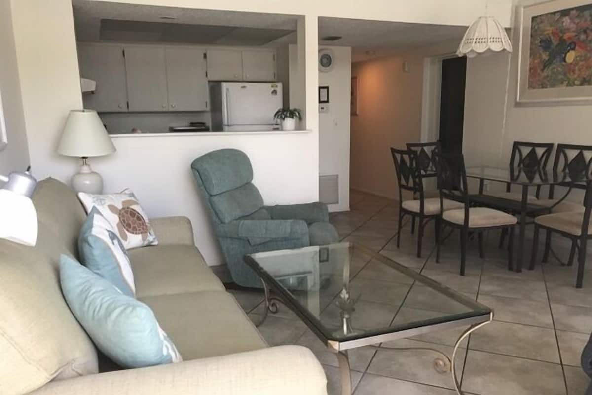 A living room with a sofa, a glass coffee table, and a dining area with a table and chairs.