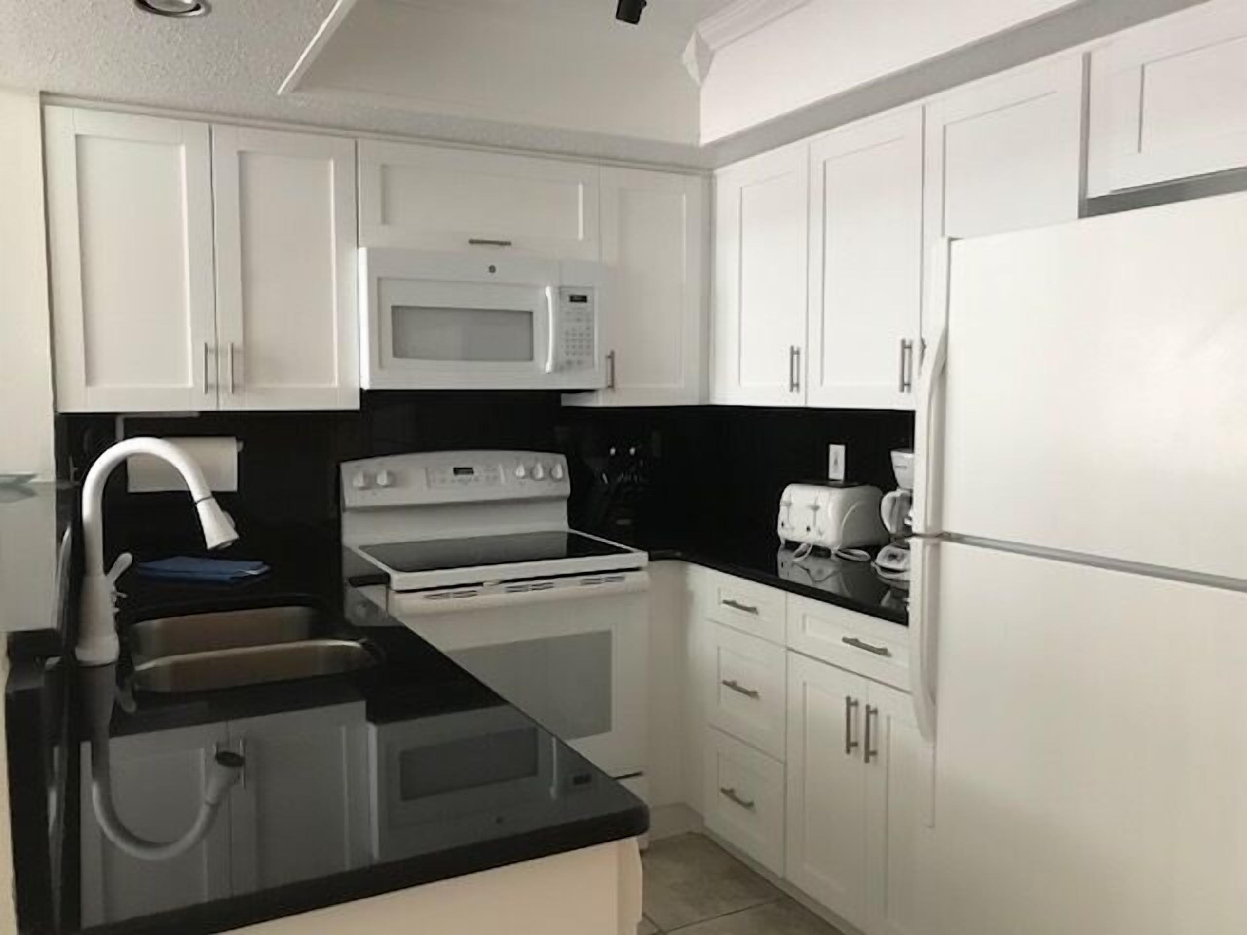 A modern kitchen with white cabinets, a black countertop, a microwave, a stove, and a refrigerator.