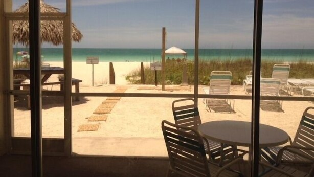 A beach view from a covered patio with a table and chairs, a thatched umbrella, and beach chairs. - Coconuts Beach Resort (Holmes Beach)