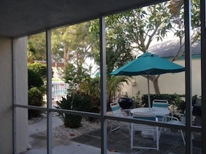 Un espace patio aménagé avec une table et des chaises, un parasol vert, et une vue sur les arbres et les bâtiments environnants.
