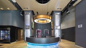 A modern reception area with a curved desk, a digital display, and a vending machine. - Aloft by Marriott Manhattan Downtown - Financial District (New York)