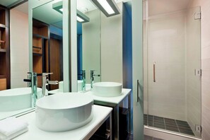 Une salle de bain moderne avec deux grands lavabos blancs, une douche en verre et un miroir qui reflète la pièce.