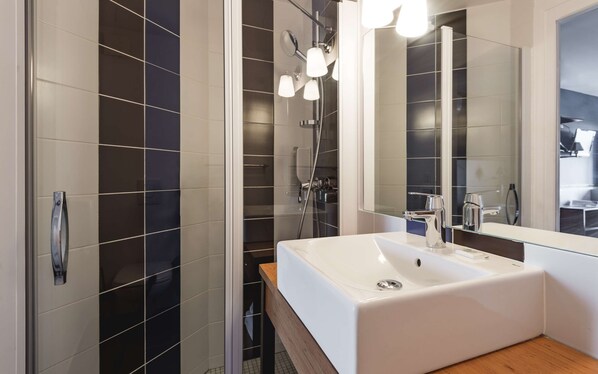 A modern bathroom with a large mirror, a white sink, and a shower with multiple lights.