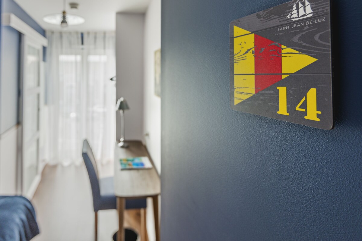 A hotel room with a bed, a desk, and a wall-mounted sign indicating room number 14.