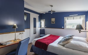 A hotel room with a bed, a desk, a chair, a window, and a ceiling light.
