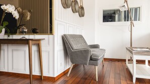 A room with a wooden floor, a grey upholstered armchair, a small table, a globe on a shelf, and a mirror on the wall. - Brit Hotel De Paris (Saint-Jean-de-Luz)