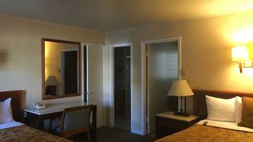 Ein Hotelzimmer mit zwei Betten, einem Schreibtisch, einem Stuhl, einem Spiegel und einer Lampe.