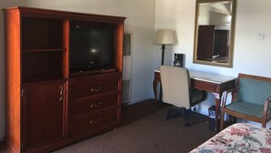 A hotel room with a wooden cabinet, a desk, a chair, a bed, a lamp, and a mirror. - Pacific Heights Inn (San Francisco)