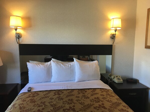 Una camera d'albergo con un letto, due lampade ai comodini, un telefono e un tavolino di fianco al letto.