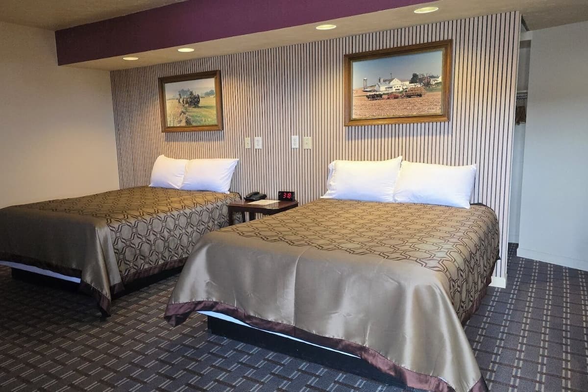 A hotel room with two beds, striped wallpaper, and two framed pictures on the wall.