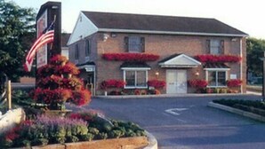 Un edificio de ladrillo de dos pisos con una entrada central, una bandera y macetas con flores.