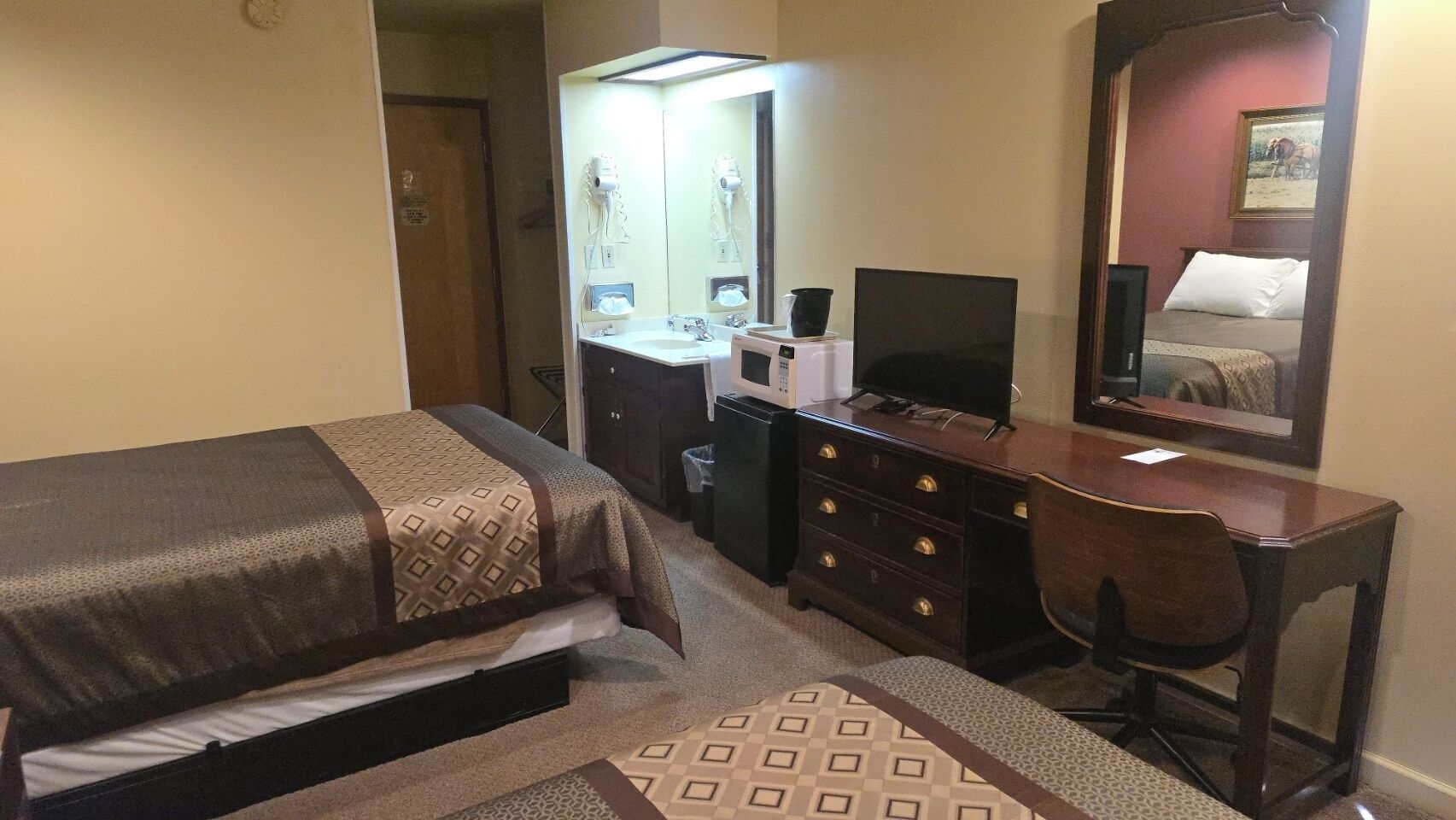 Une chambre d’hôtel comprenant un lit, un bureau, une commode, un miroir et un téléviseur.