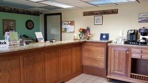 Una zona de recepción con mostrador de madera, una máquina de café y un tablón de anuncios con diversos avisos.