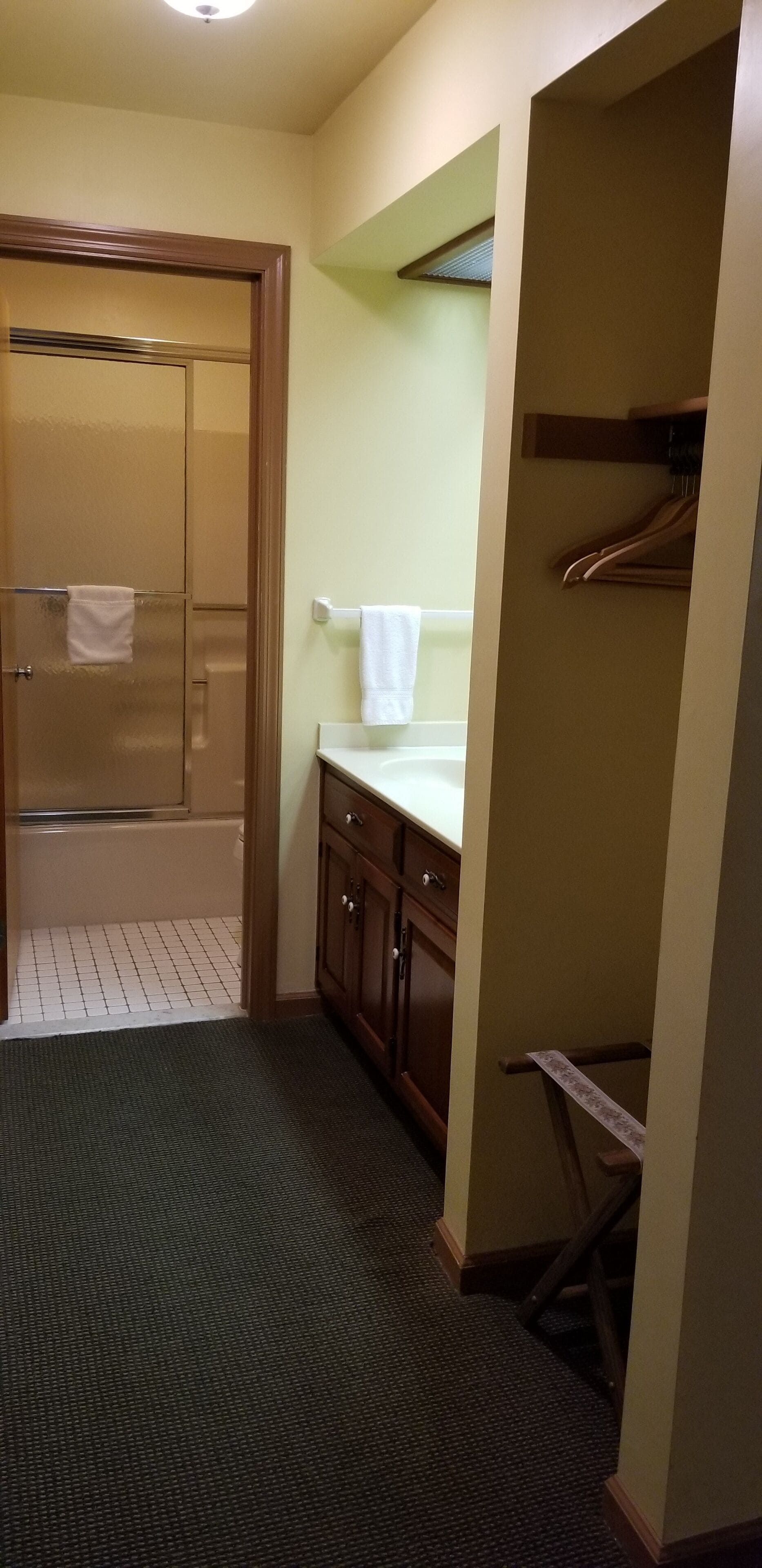 Un baño con mampara de vidrio, lavamanos con espejo y un perchero para toallas.