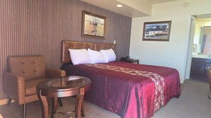 A hotel room with a large bed, a chair, a small table, and two framed pictures on the wall.