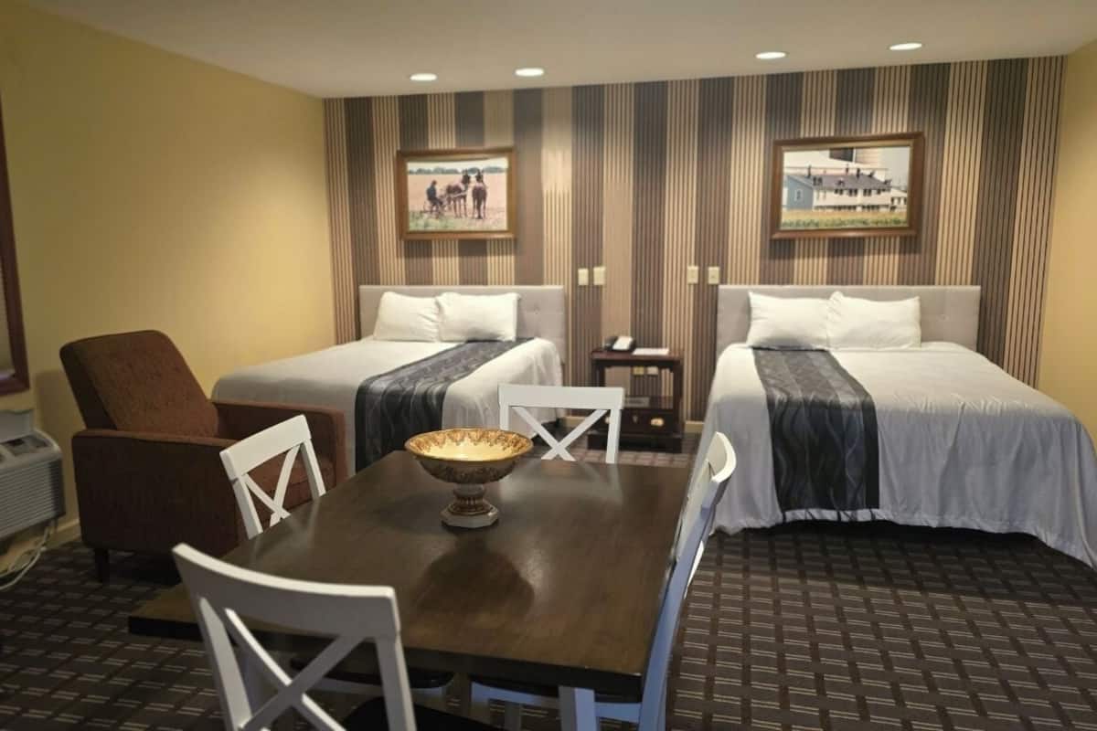 A hotel room with two beds, a dining table, and a chair.