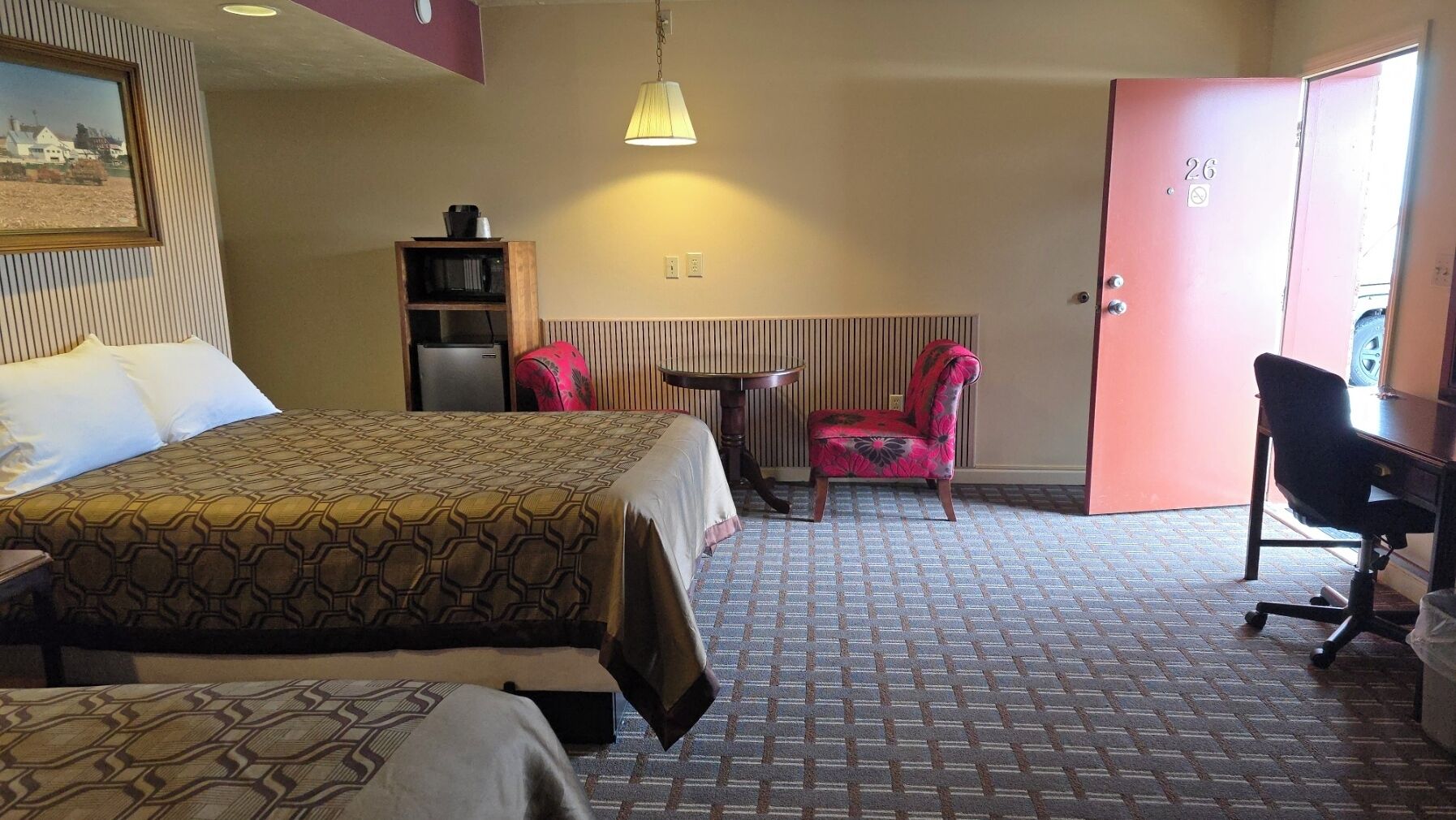 A hotel room with a bed, a desk, a chair, a small table, and a radiator.