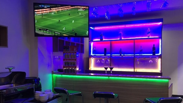 A bar area with a sports screen, bar stools, and a counter with bottles. - Good Luck Hotel (Yangon)