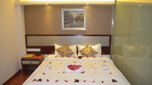 A hotel room with a large bed, a bedside table with a phone, and a painting on the wall. - Good Luck Hotel (Yangon)