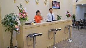 A reception desk with a TV screen, clocks, and potted plants. - Good Luck Hotel (Yangon)