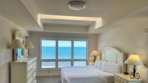 A bedroom with a large window offering a view of the sea, a bed with white linens, a dresser, and two bedside lamps. - The Beach Haus Resort (Traverse City)