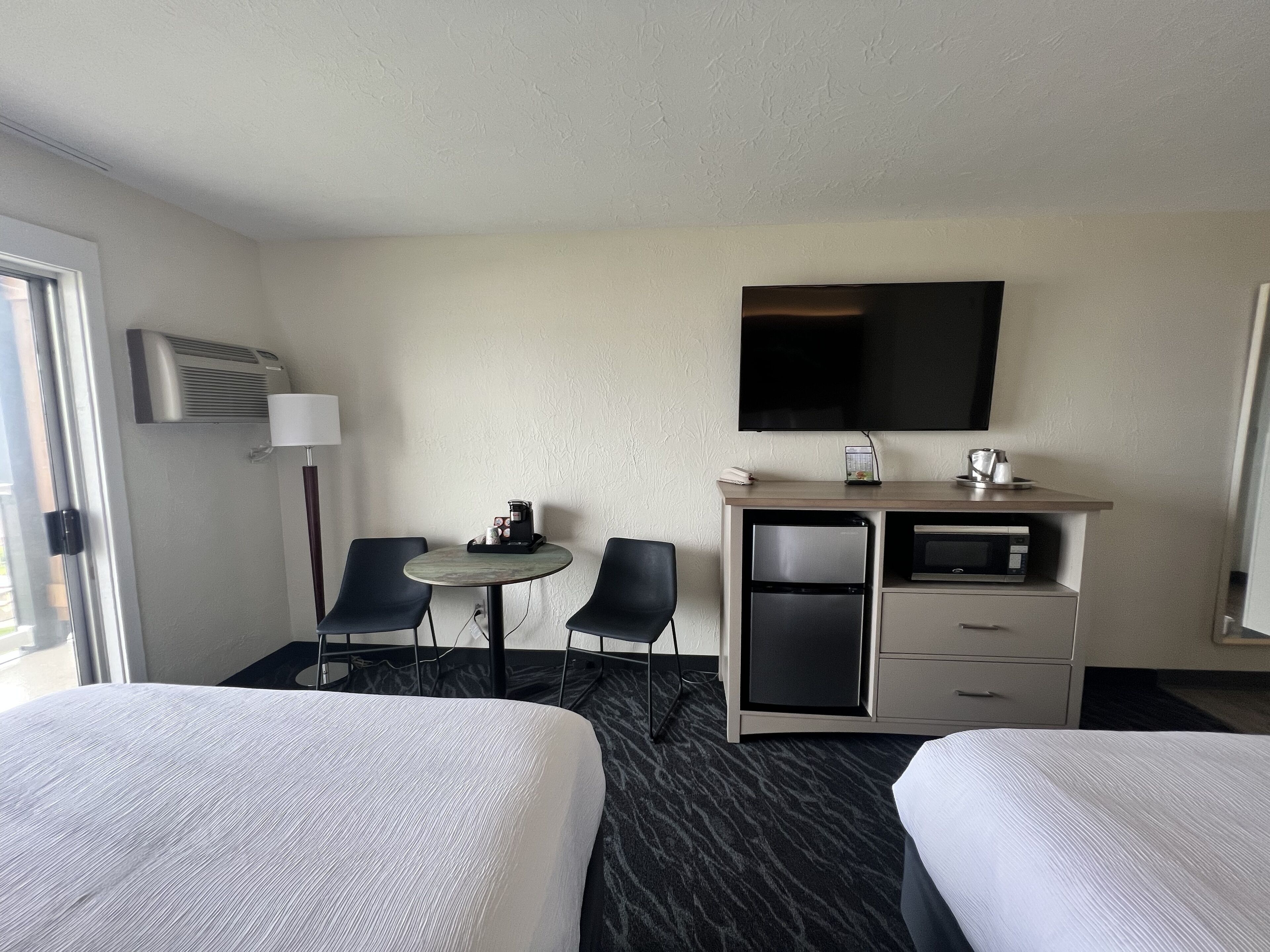 A hotel room with two beds, a small table with a coffee maker, a refrigerator, a microwave, and a TV mounted on the wall.