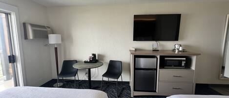 A hotel room with two beds, a small table with a coffee maker, a refrigerator, a microwave, and a TV mounted on the wall.