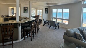 A spacious kitchen with a large island and bar seating, a dining area with chairs, and a view of the water through large windows. - The Beach Haus Resort (Traverse City)