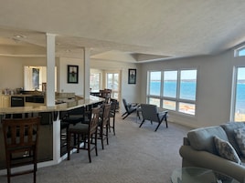 A spacious kitchen with a large island and bar seating, a dining area with chairs, and a view of the water through large windows.