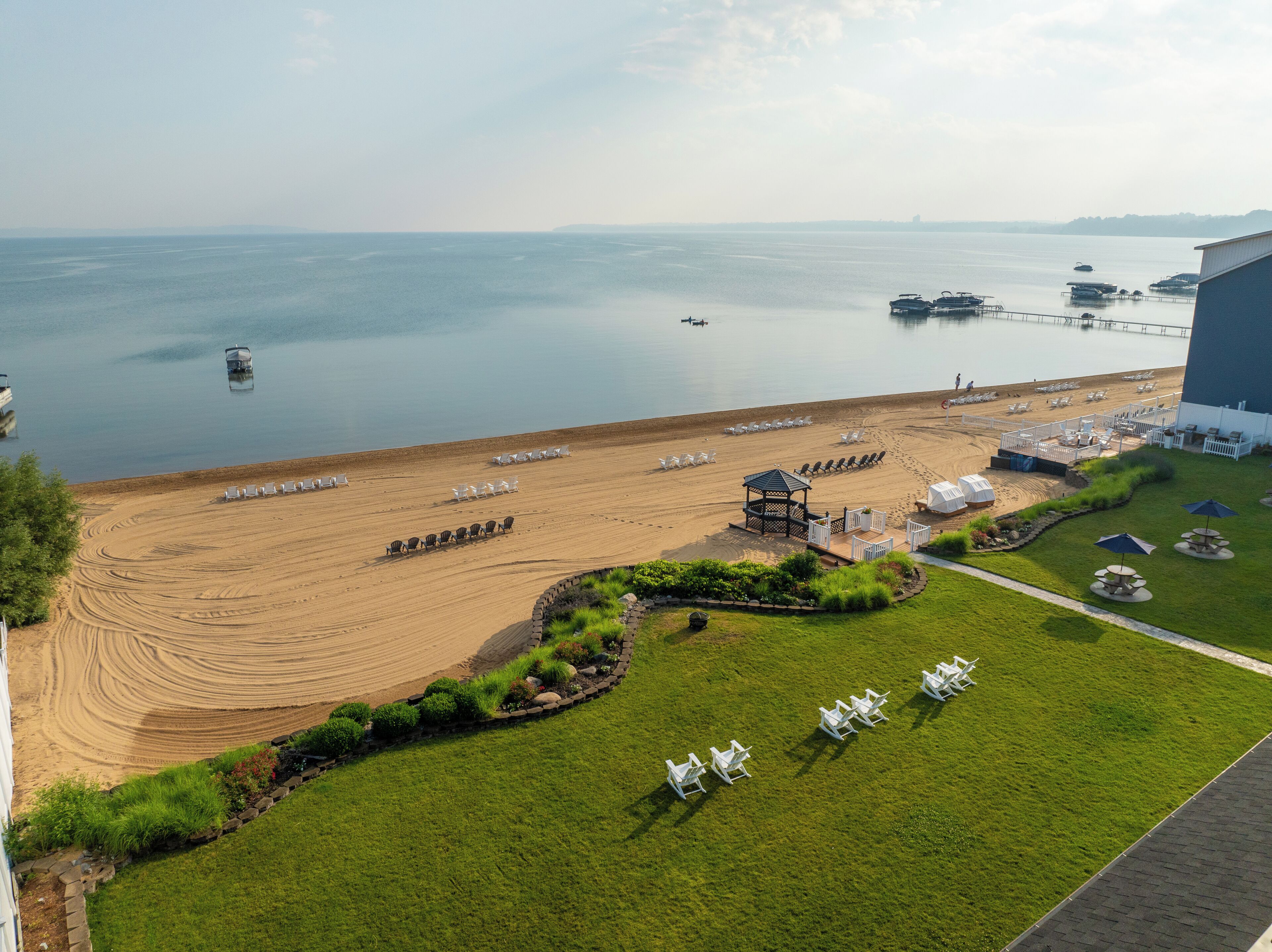 Ein Hotel direkt am Strand mit Sand, Liegestühlen, einer Laube und Meerblick.