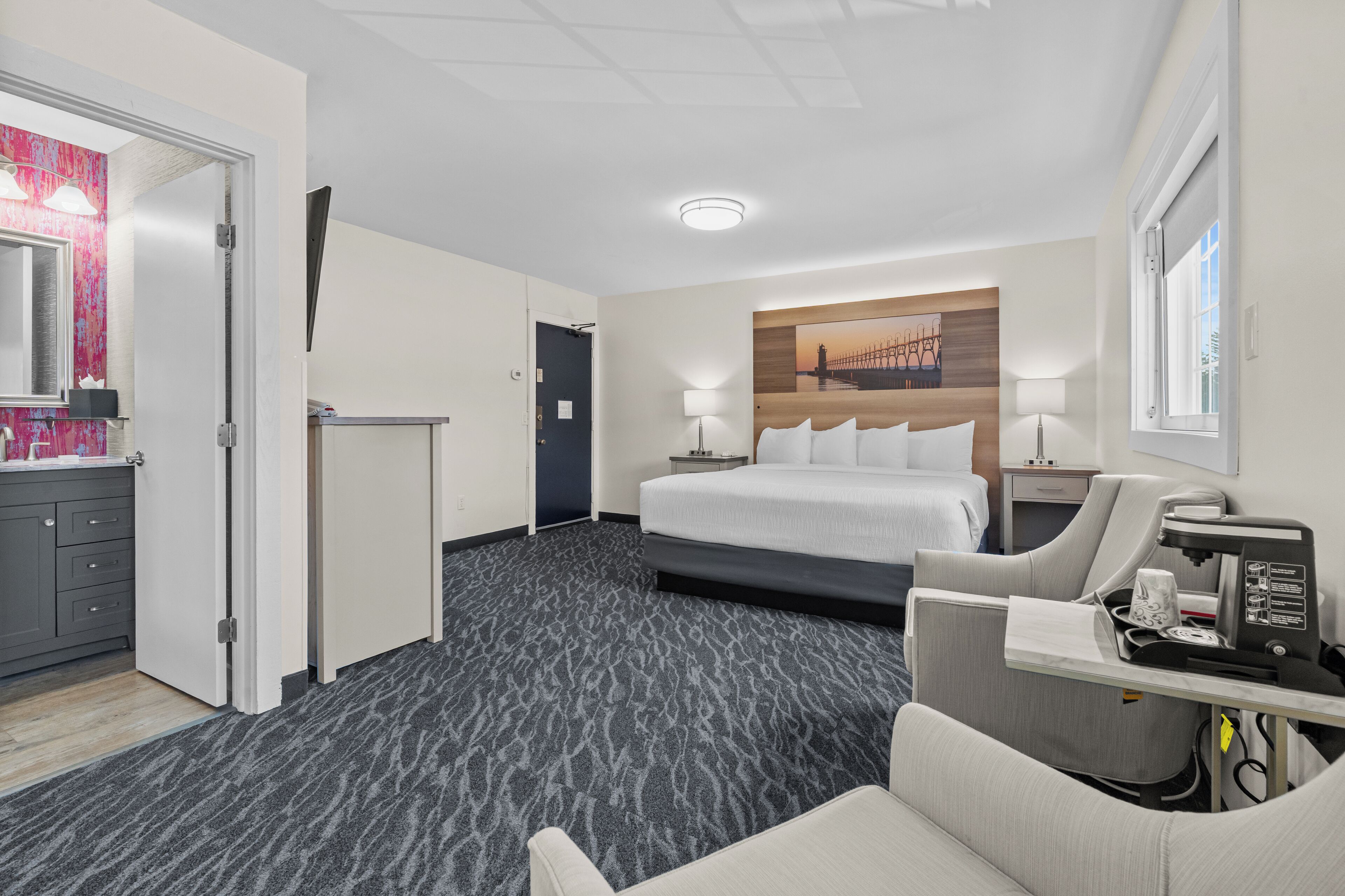 Ein Hotelzimmer mit einem Bett, Nachttischen, einem Schreibtisch, einem Sessel und einem Wandbild.
