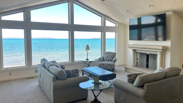 A living room with large windows overlooking the sea, a fireplace, and a ceiling fan. - The Beach Haus Resort (Traverse City)