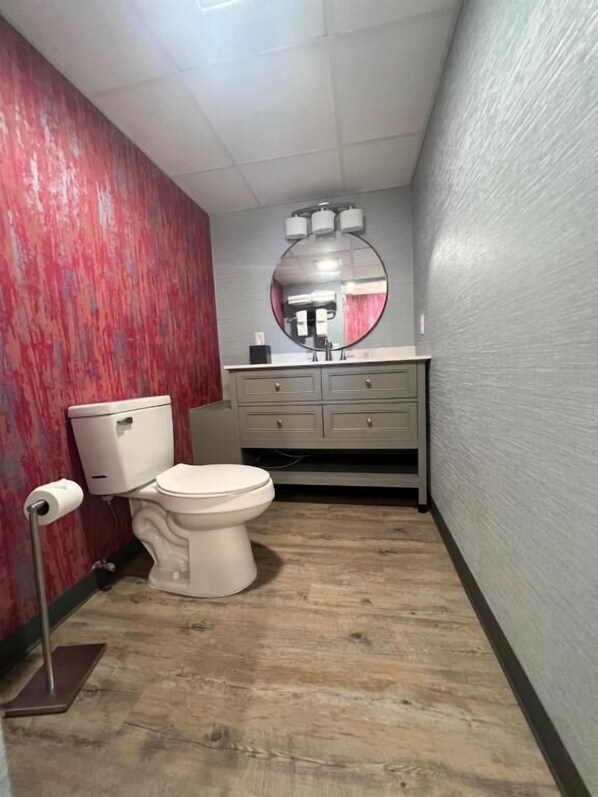 Un baño con inodoro, tocador con espejo y un rollo de papel higiénico en el suelo.