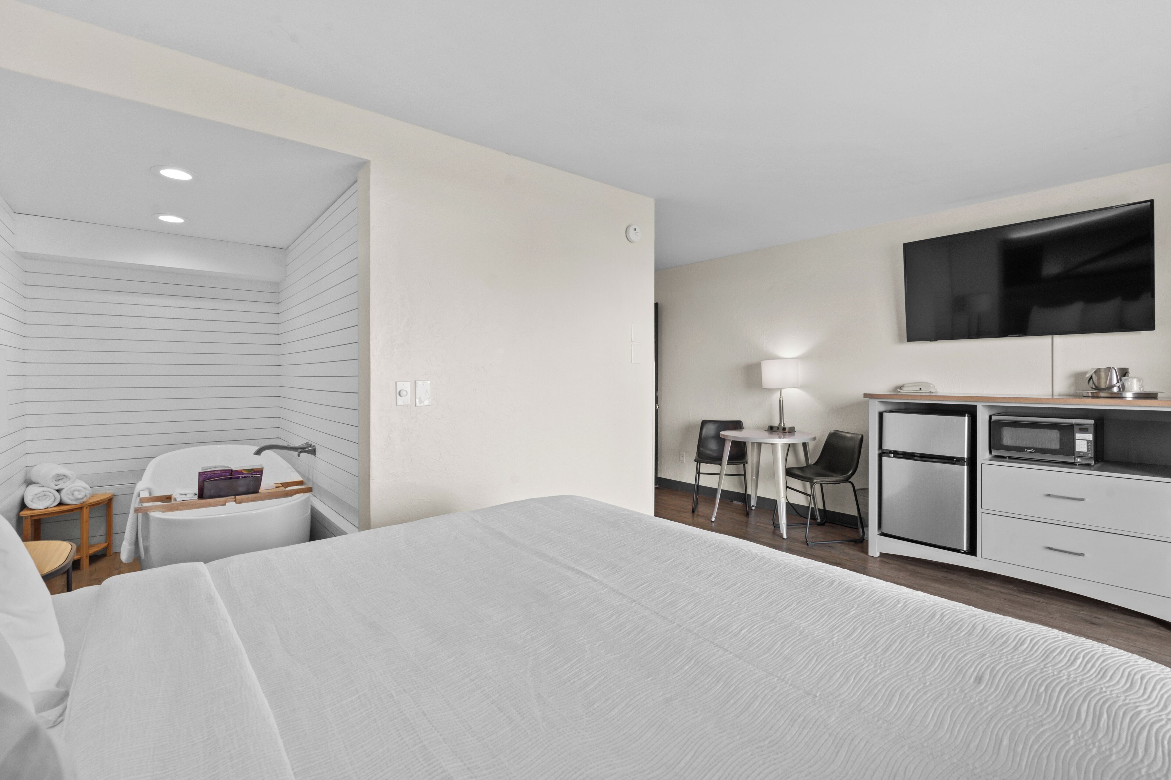 A modern hotel room with a large bed, a desk with a computer, a microwave, and a flat-screen TV.