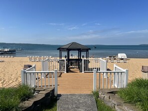 Relax on the beachside deck, surrounded by lounge chairs and tables, with the calm sea and clear sky in the background.