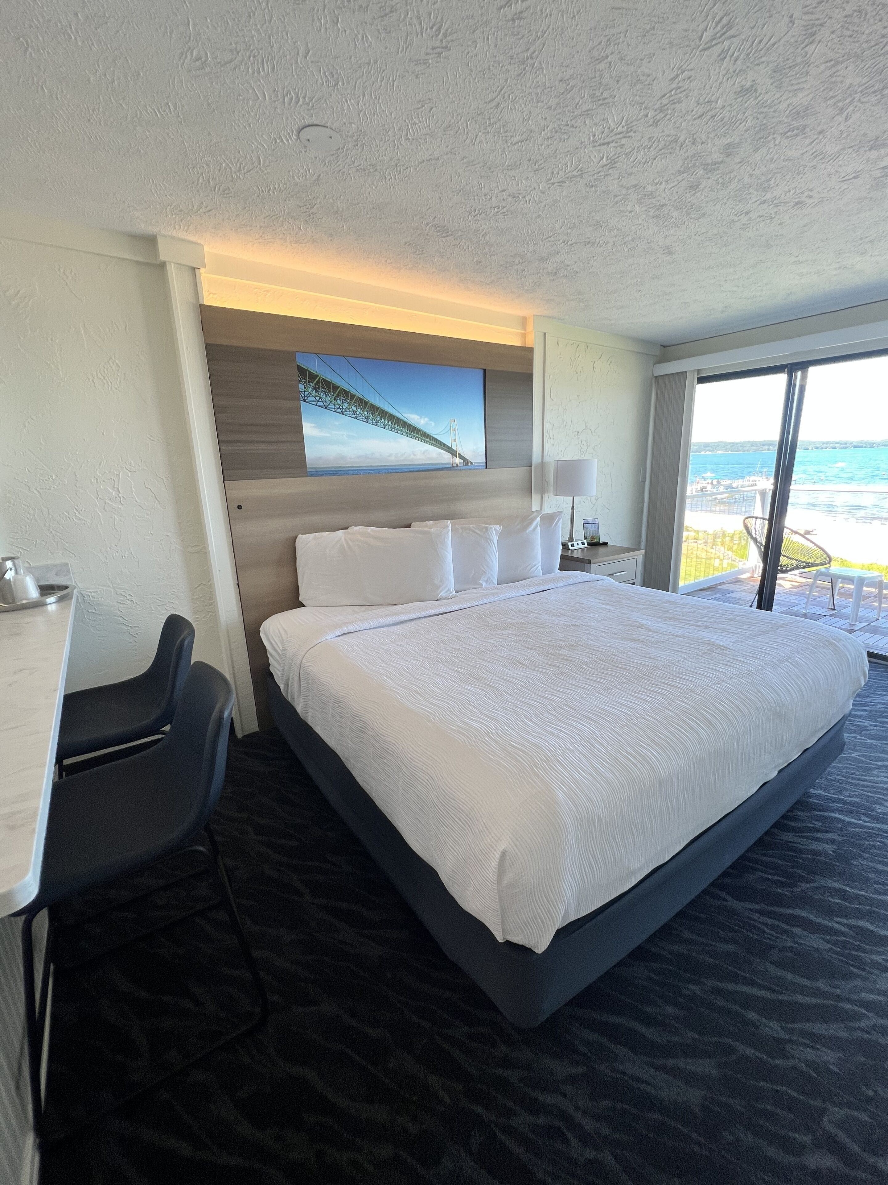 Une chambre d’hôtel avec un grand lit, un bureau et une chaise. Il y a une fenêtre donnant sur la mer.