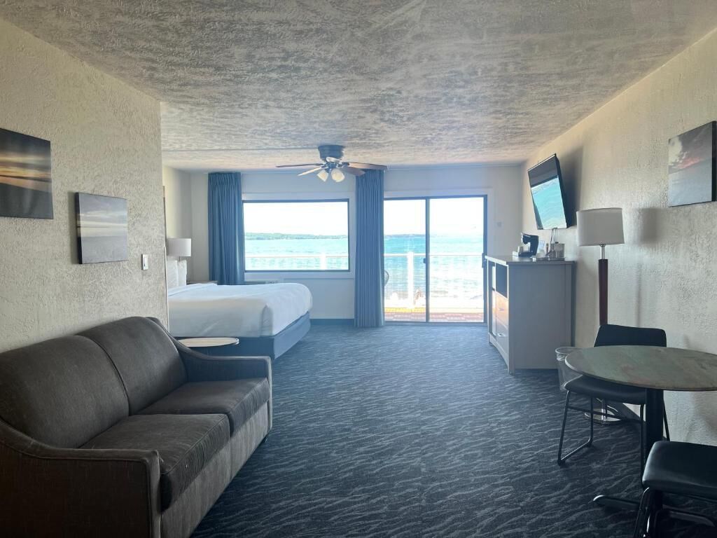 Een hotelkamer met een bed, een bank, een bureau, een televisie en uitzicht op zee.